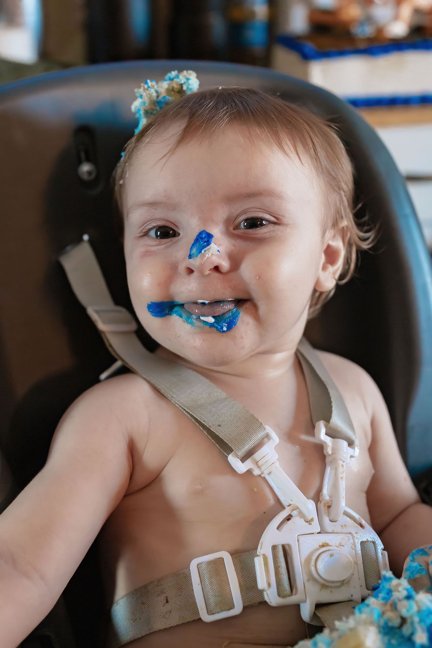 Close up of baby covered in blue birthday cake frosting during cake smash photo session.