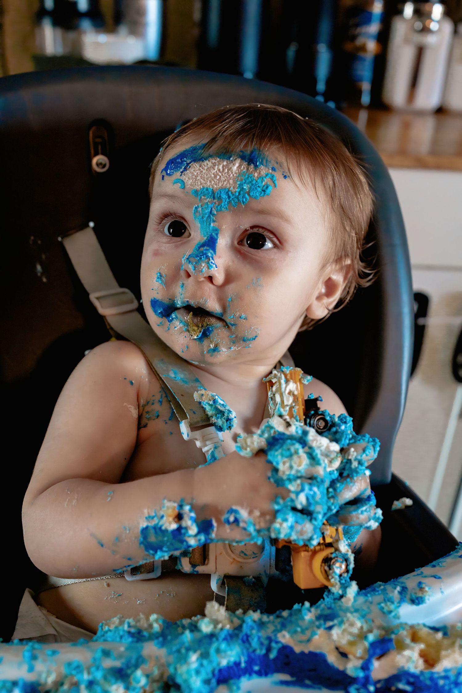Baby wearing turquoise outfit gets messy while eating bright blue cake during first birthday smash cake photoshoot.