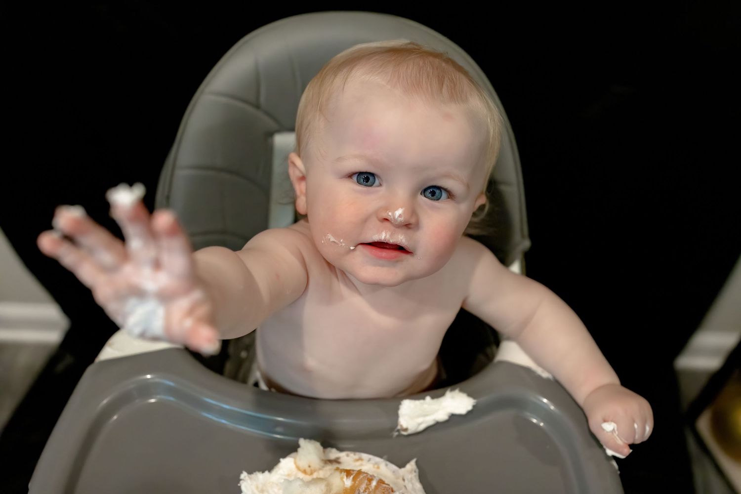 Smiling baby in high chair celebrating with gold party decorations.