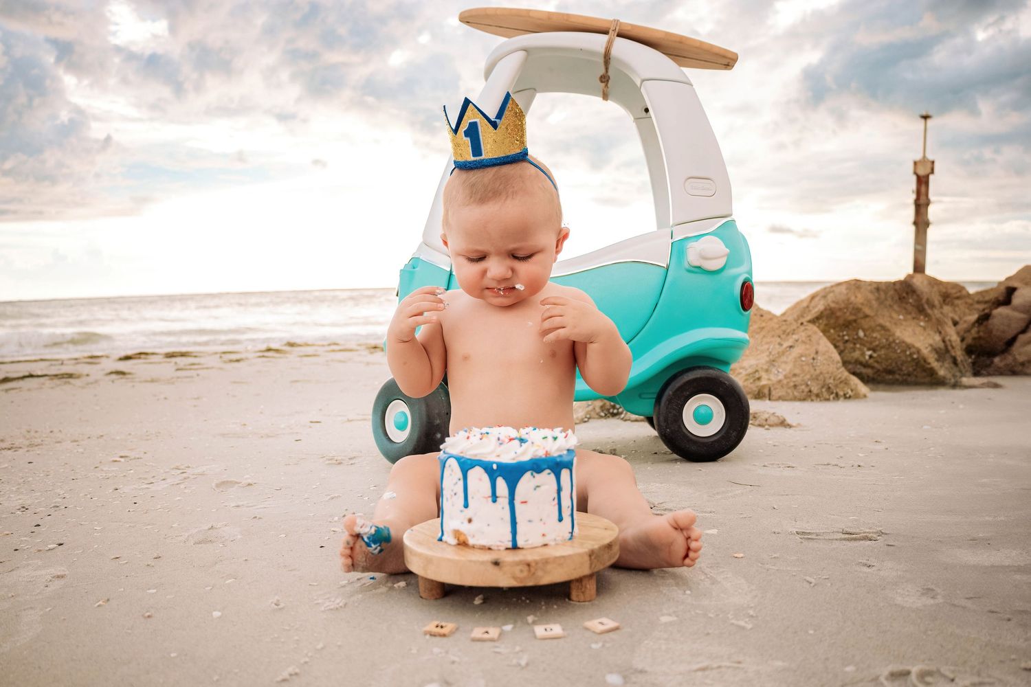 Beachside first birthday cake smash setup with turquoise toy car and wooden cake stand.