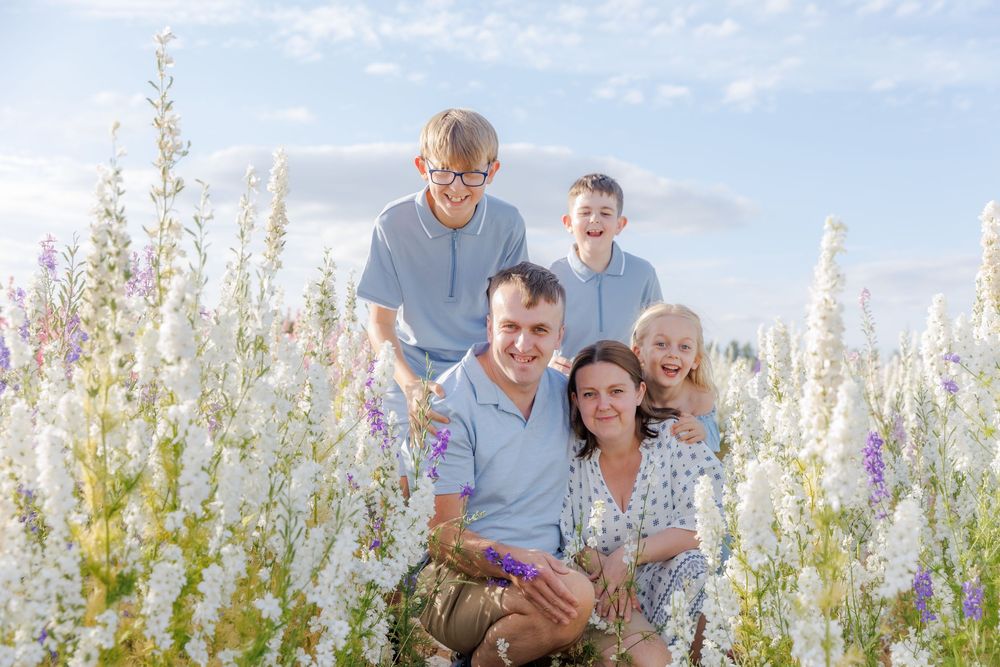 A family of three poses together in a field of purple wildflowers during a golden summer sunset.