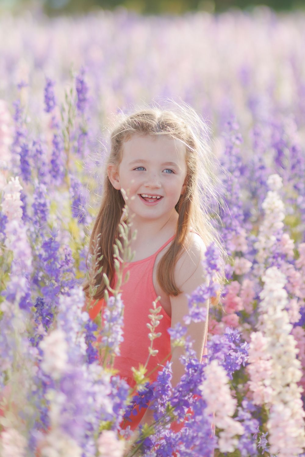 A joyful moment captured in a blooming field of purple and pink delphinium flowers on a sunny summer day.