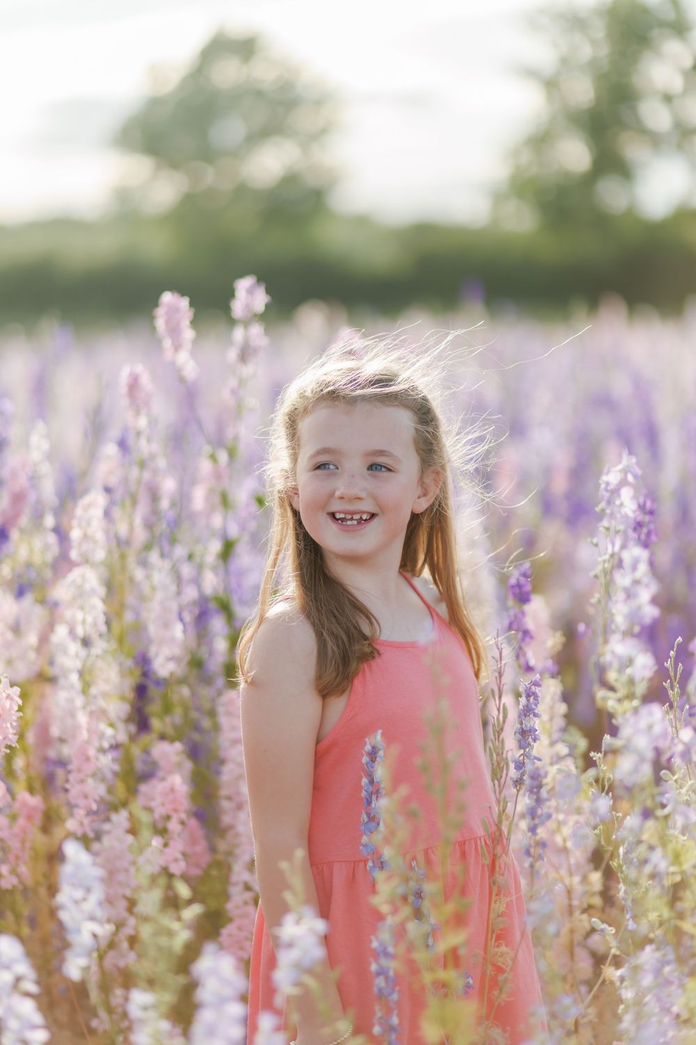 A coral sundress stands out among blooming purple wildflowers in a sunlit meadow during golden hour.