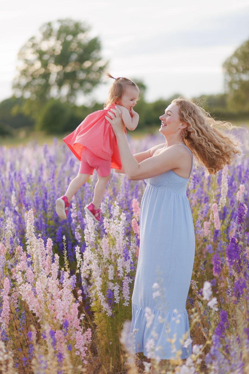 A child in a blue dress dances and spins through a field of purple and pink wildflowers at sunset.
