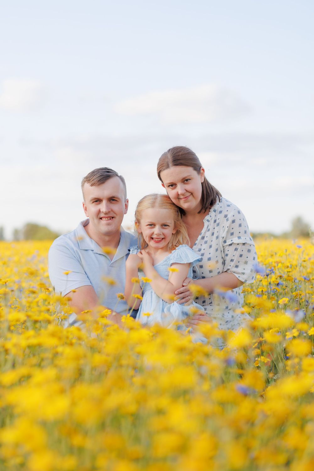 A family shares joyful moments together while laying in a vibrant field of yellow wildflowers on a sunny day.