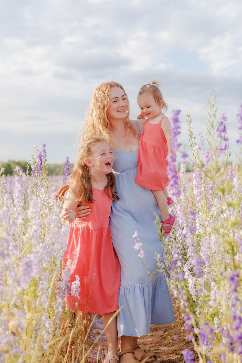 A mother and daughter share joyful moments in a field of delicate purple wildflowers on a summer day.