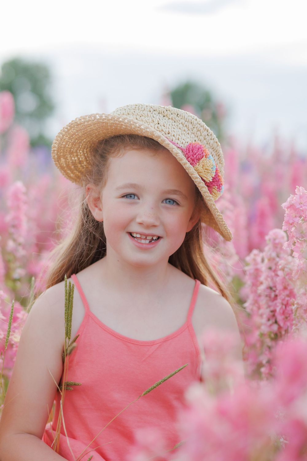 A straw hat adorned with pink flowers rests atop long hair in a vibrant field of pink astilbe blooms.