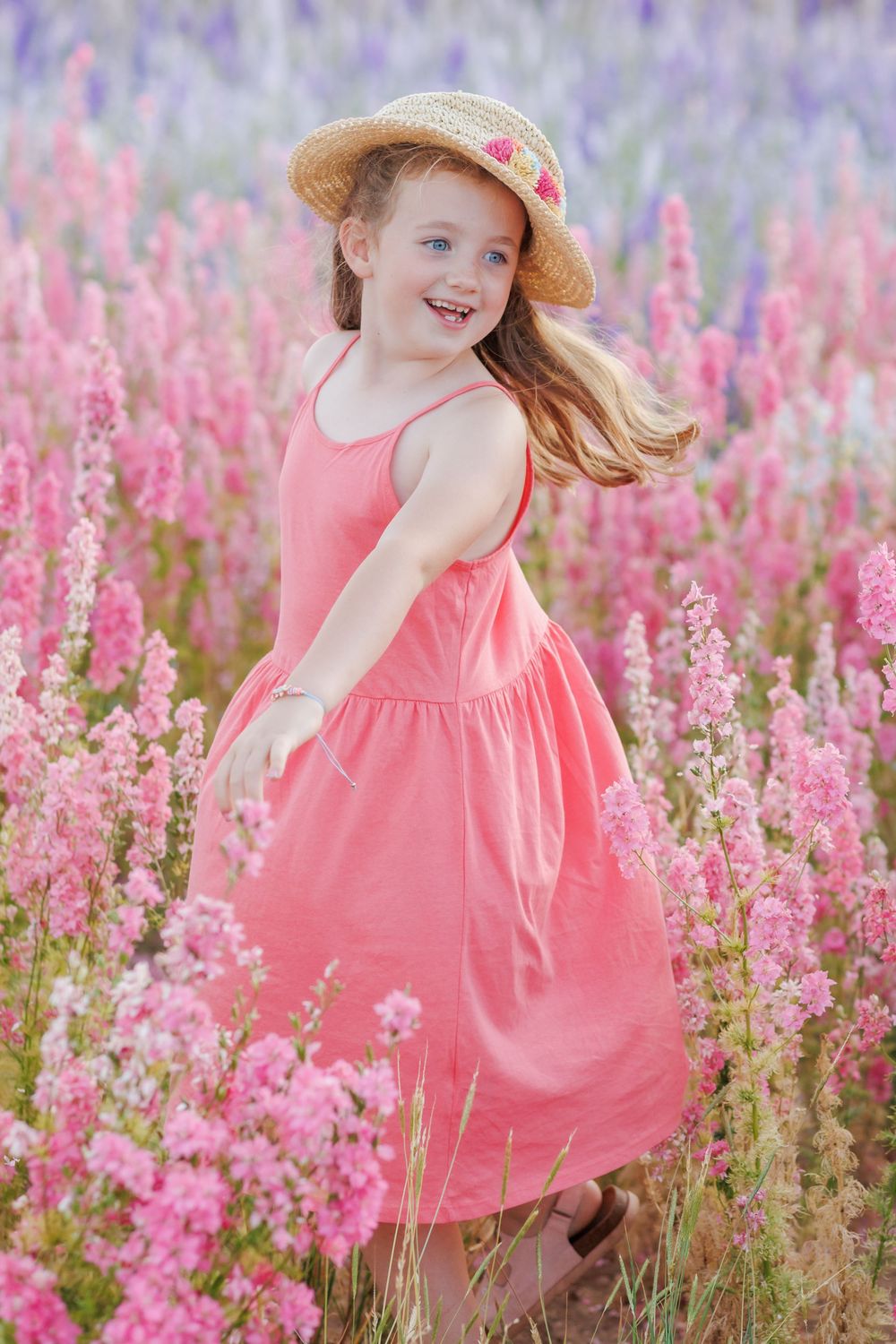 A cheerful moment in a field of pink flowers with a coral dress and straw hat creating a dreamy summer scene.