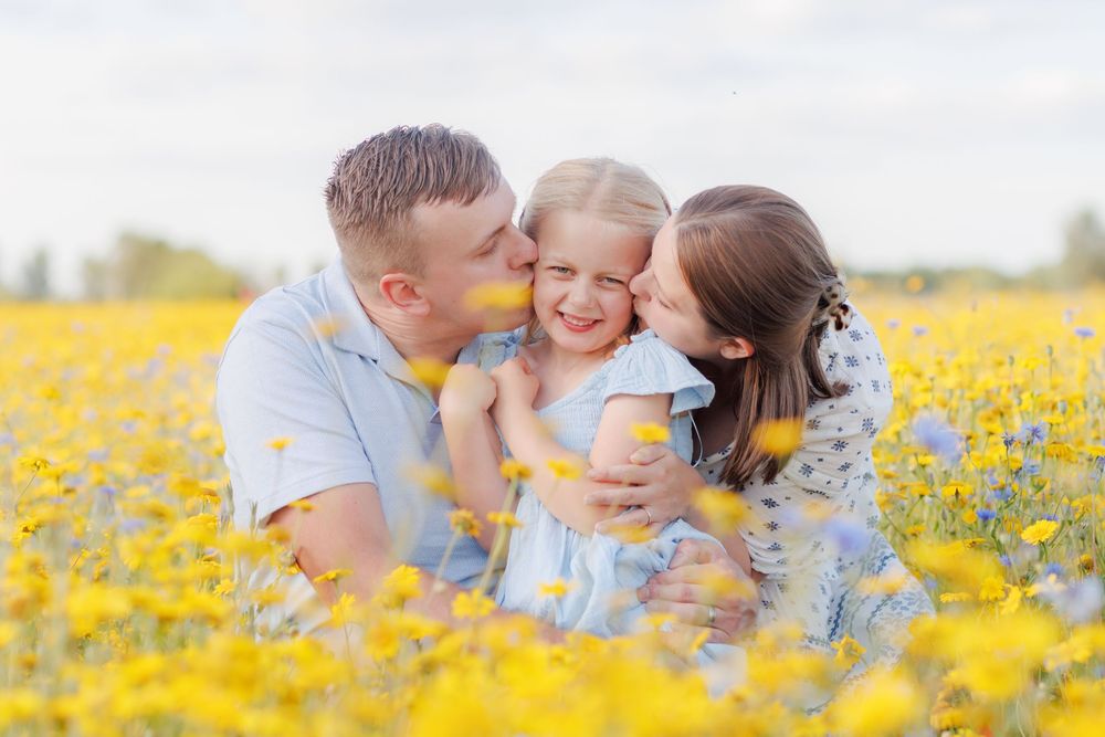Family affectionately gazes at each other while sitting in a vibrant yellow wildflower meadow on a sunny day.
