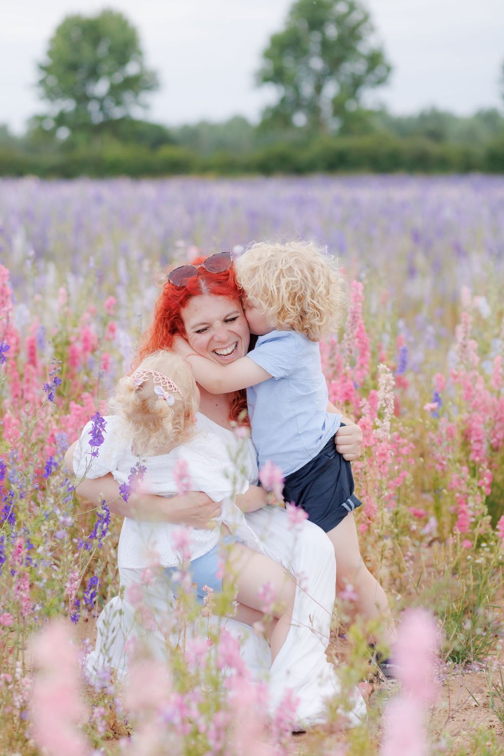 Two people in white outfits share a joyful moment surrounded by blooming purple and pink wildflowers in a summer meadow.