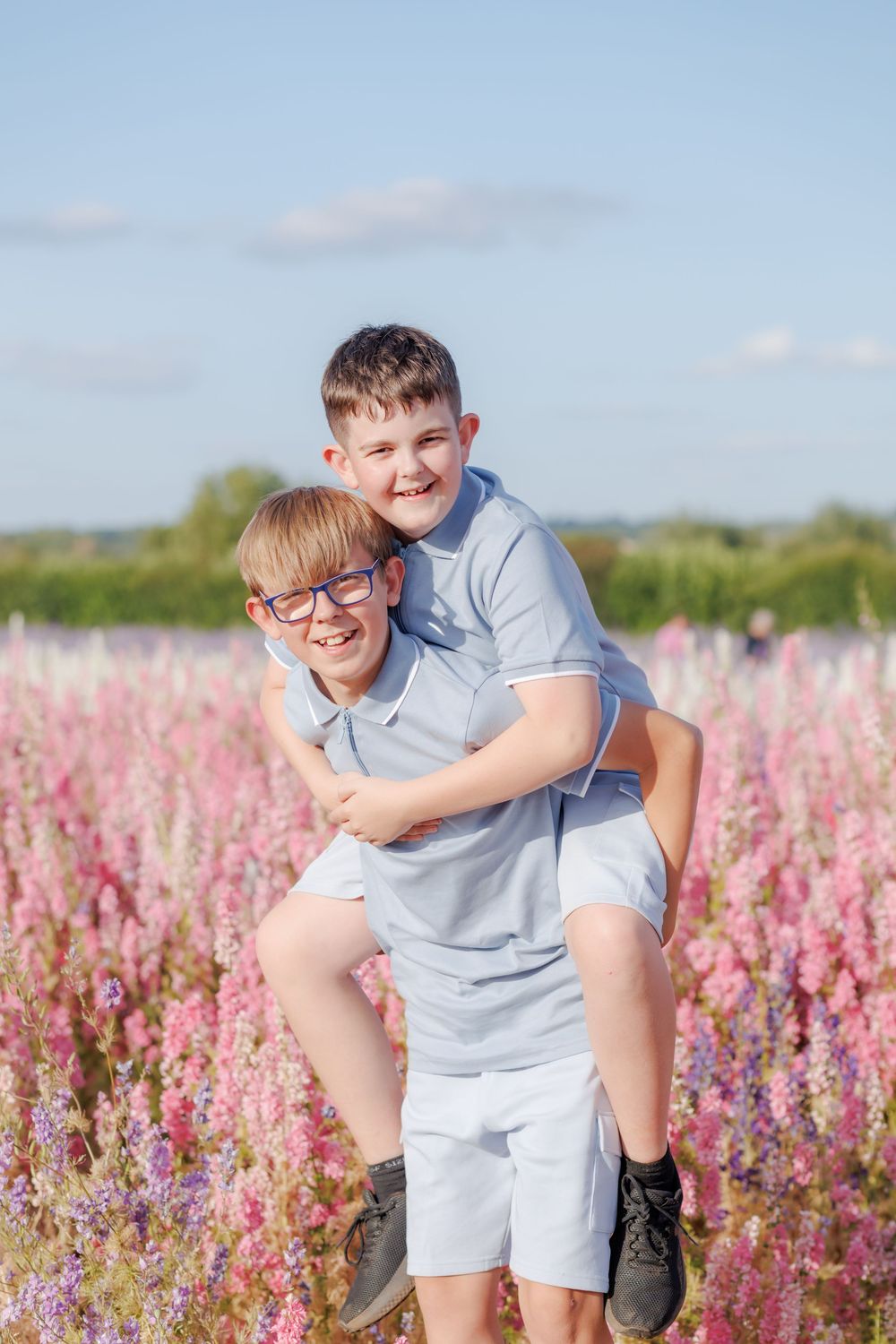 Two people playing and laughing together in a field of pink wildflowers on a sunny summer day.