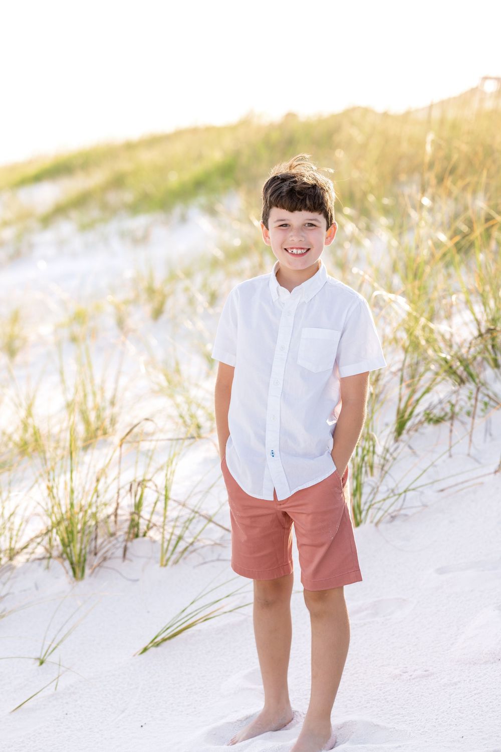 A series of candid beach portraits showing someone in white shirt and coral shorts playing in sandy dunes at sunset.
