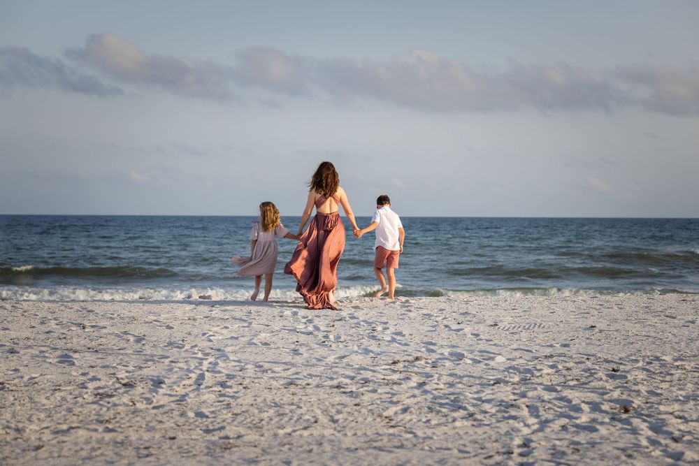 People walking along a serene white sandy beach with calm ocean waves in the background during sunset.