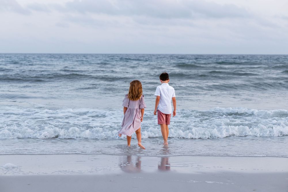 Couple walking hand in hand along the shoreline at sunset as gentle waves roll onto the sandy beach.