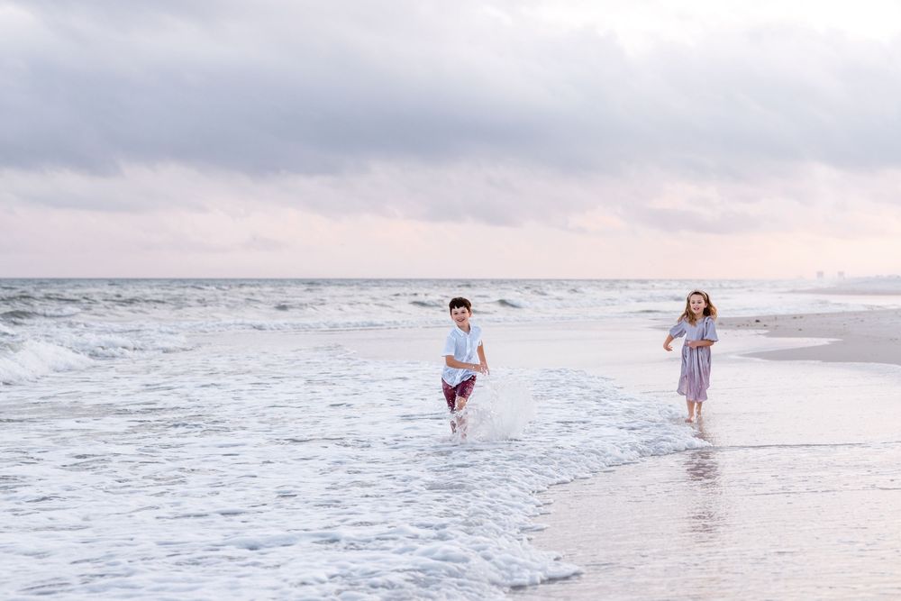 Children playing and splashing in shallow ocean waters at a peaceful beach during golden hour.