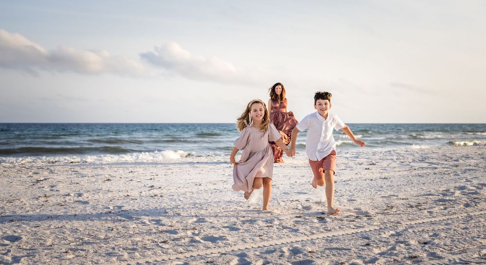 Group of people running together joyfully on a sandy beach with ocean waves in the background.