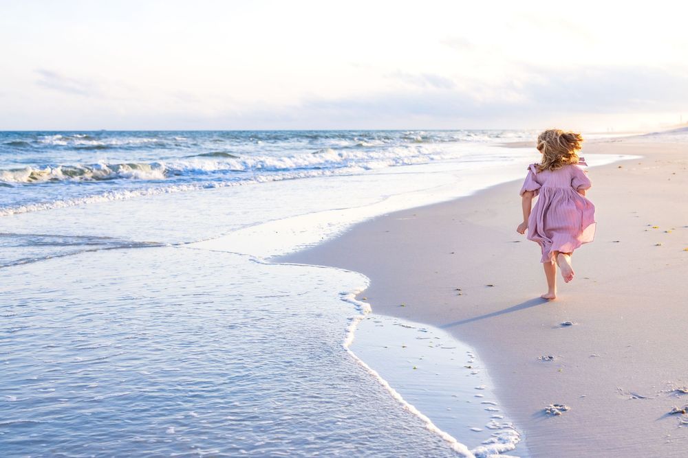 Two people stroll barefoot on a pristine white sand beach with rolling ocean waves in the background.