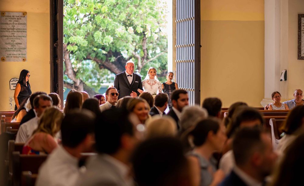A crowded indoor venue shows attendees gathered at tables while others stand near an entrance with natural lighting.