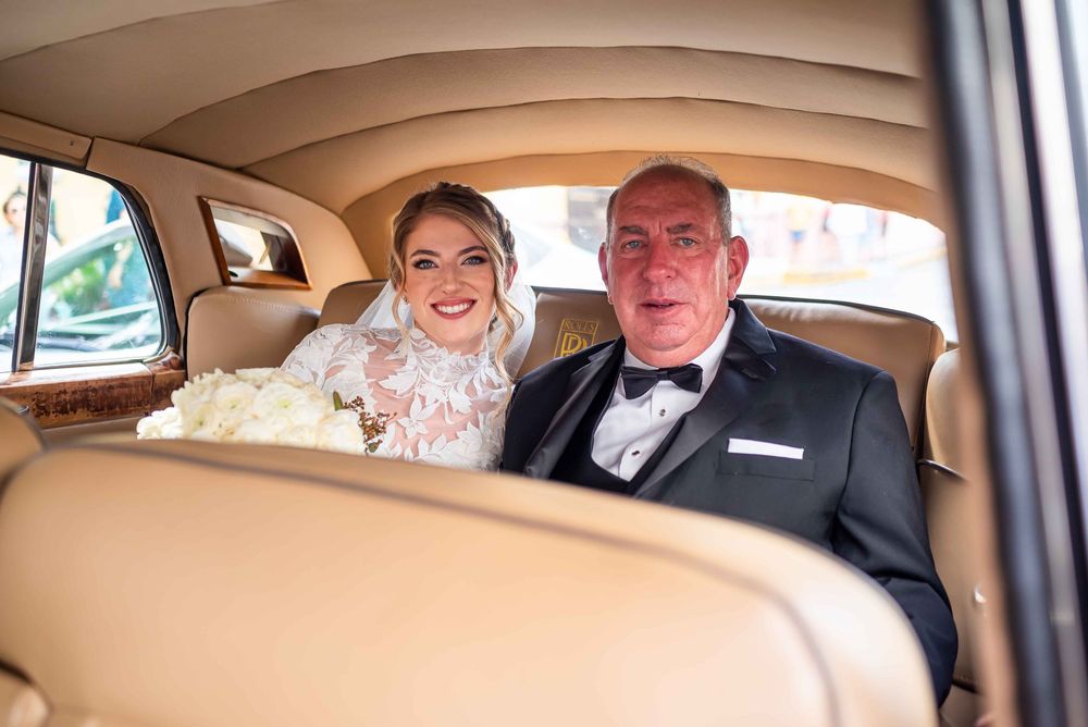 The interior of a car shows people celebrating with joyful expressions during what appears to be a wedding day.