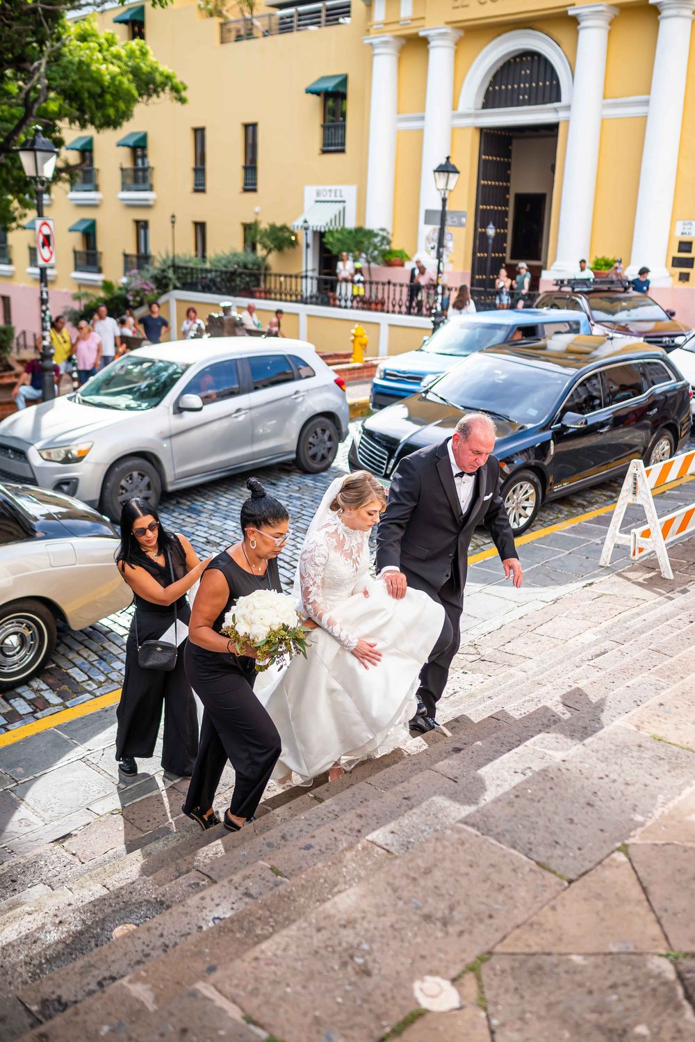 A group ascends stone stairs while helping a bride in a white gown outside a yellow colonial building in Old San Juan.