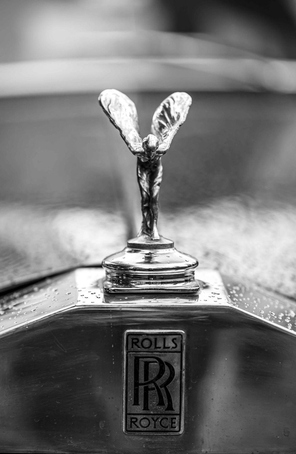 Classic Rolls-Royce Spirit of Ecstasy hood ornament in black and white against a blurred background.