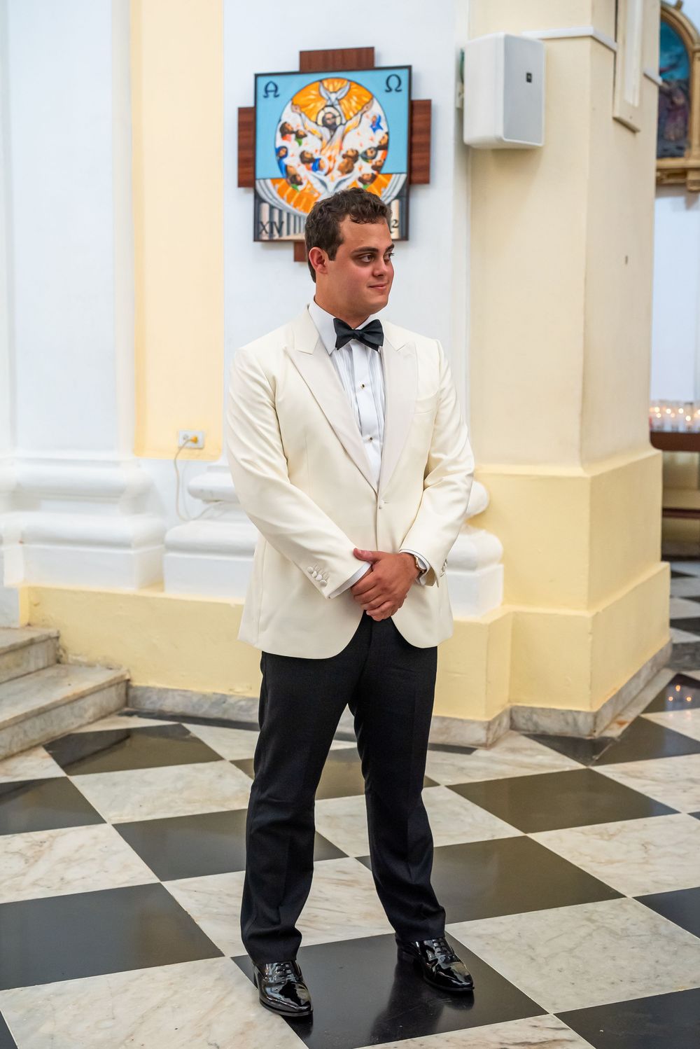 A well-dressed person in a white dinner jacket and bow tie standing on a checkered floor.