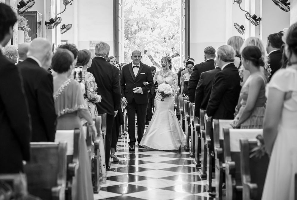 Black and white photograph of traditional church ceremony with guests seated in wooden pews.