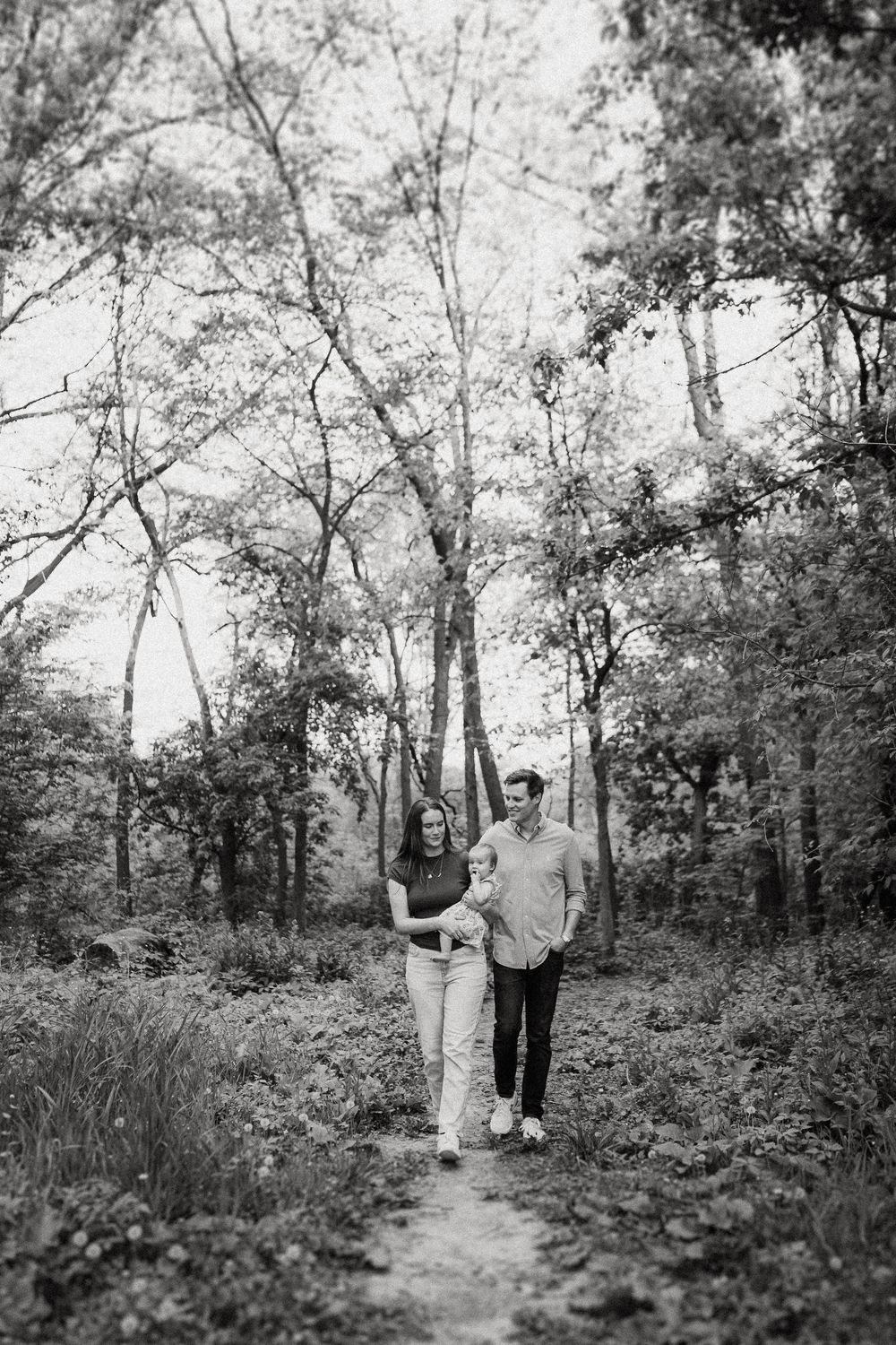 A couple takes a romantic stroll together on a wooded trail in black and white.