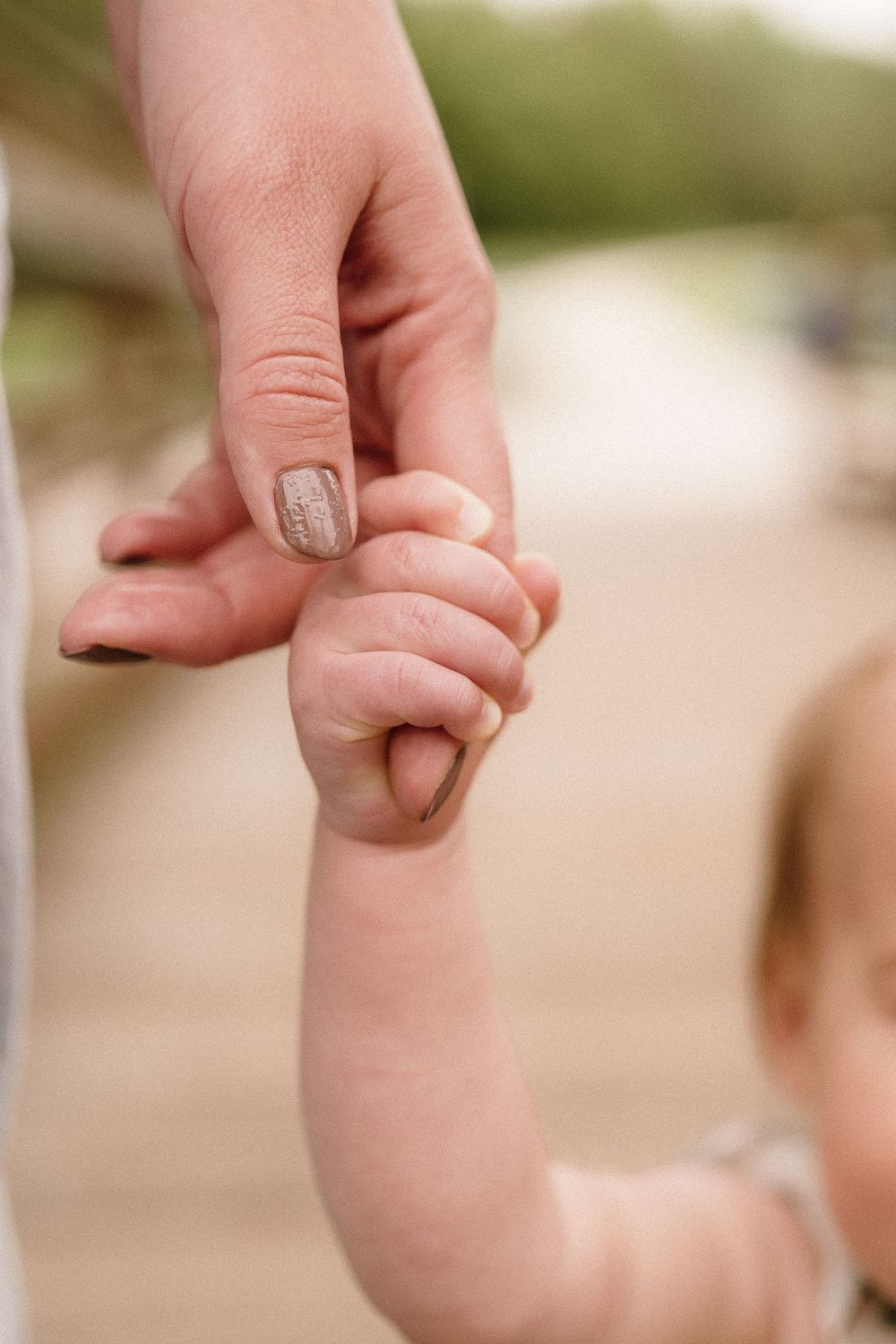 Close-up of adult and child's hands holding each other with painted fingernails visible.