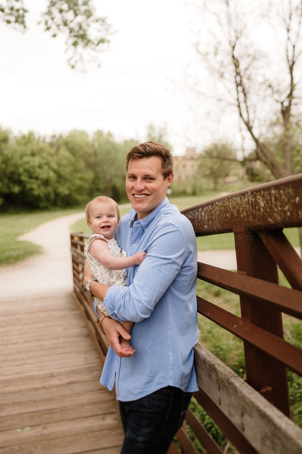 Parent holding child while standing on wooden bridge in park setting.