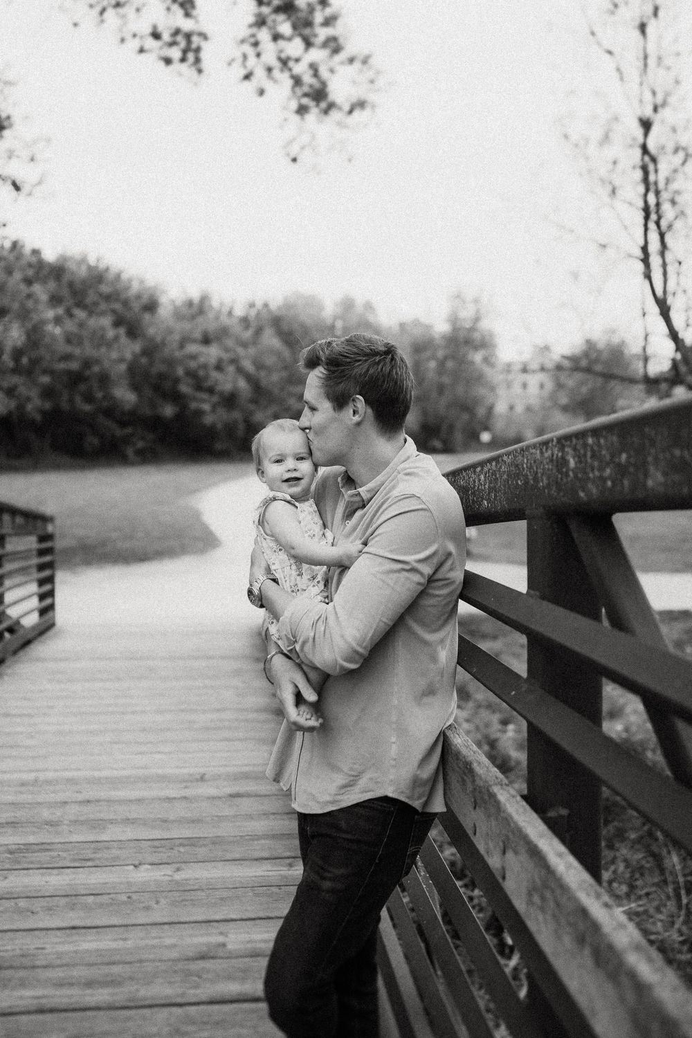 Black and white portrait of a tender moment between parent and baby on a wooden bridge walkway.