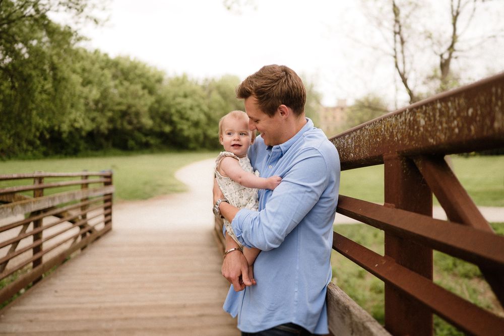 A sweet candid portrait of a parent holding a baby while standing on a wooden bridge outdoors.