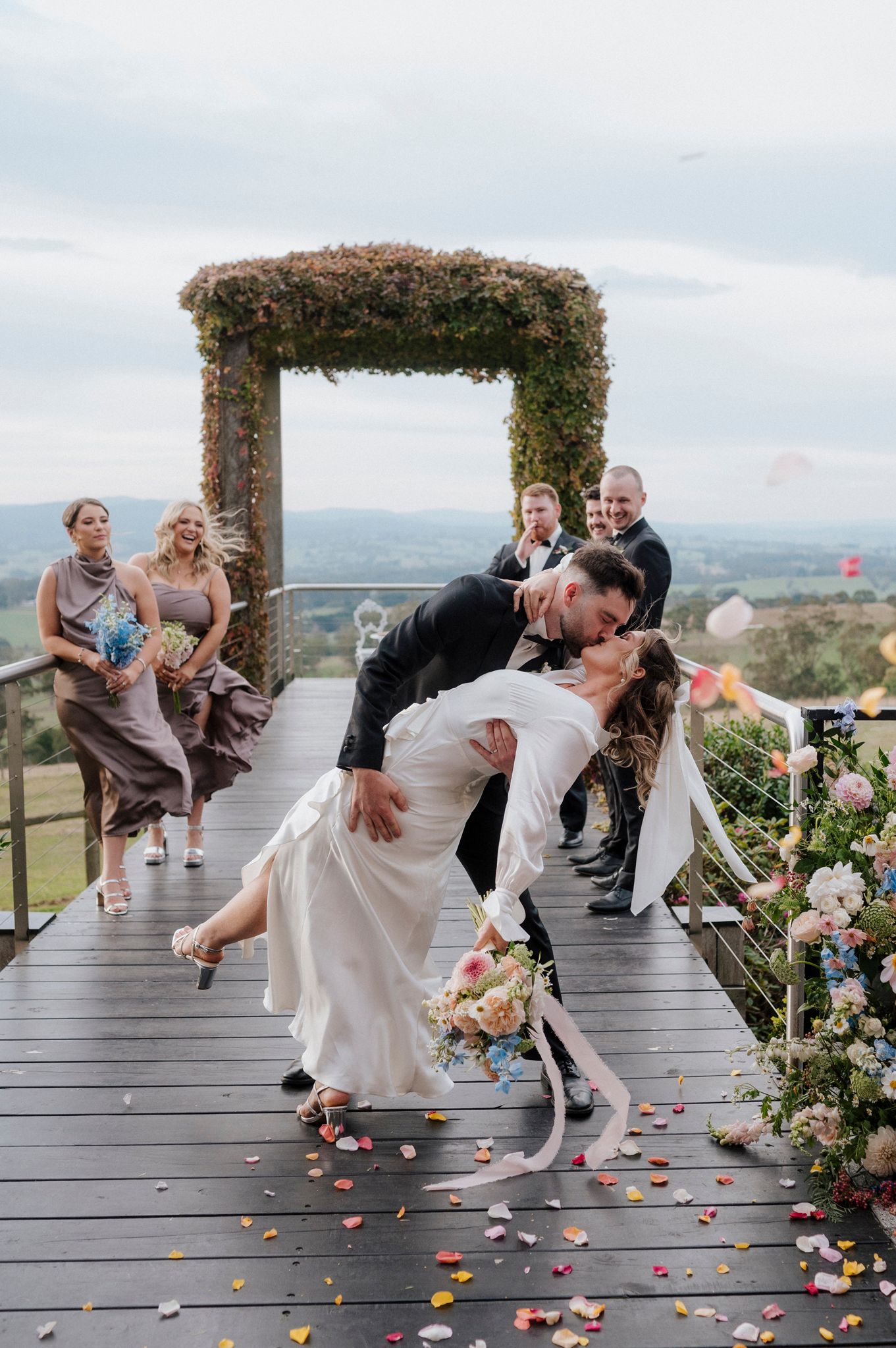 Wedding couple performs dramatic dip pose on decorated deck with flower petals.