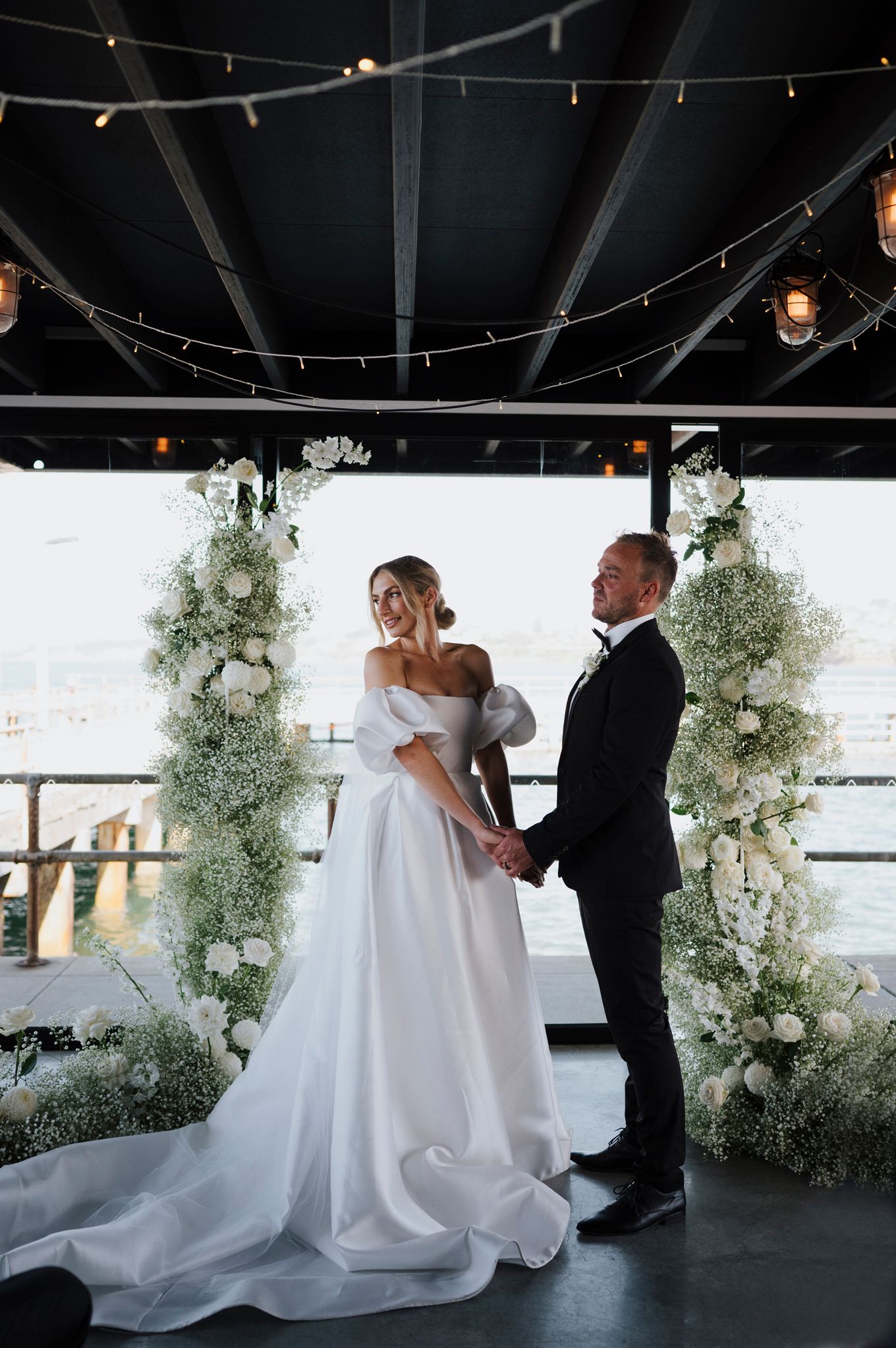 Wedding couple dances under string lights with floral arch and elegant decor.