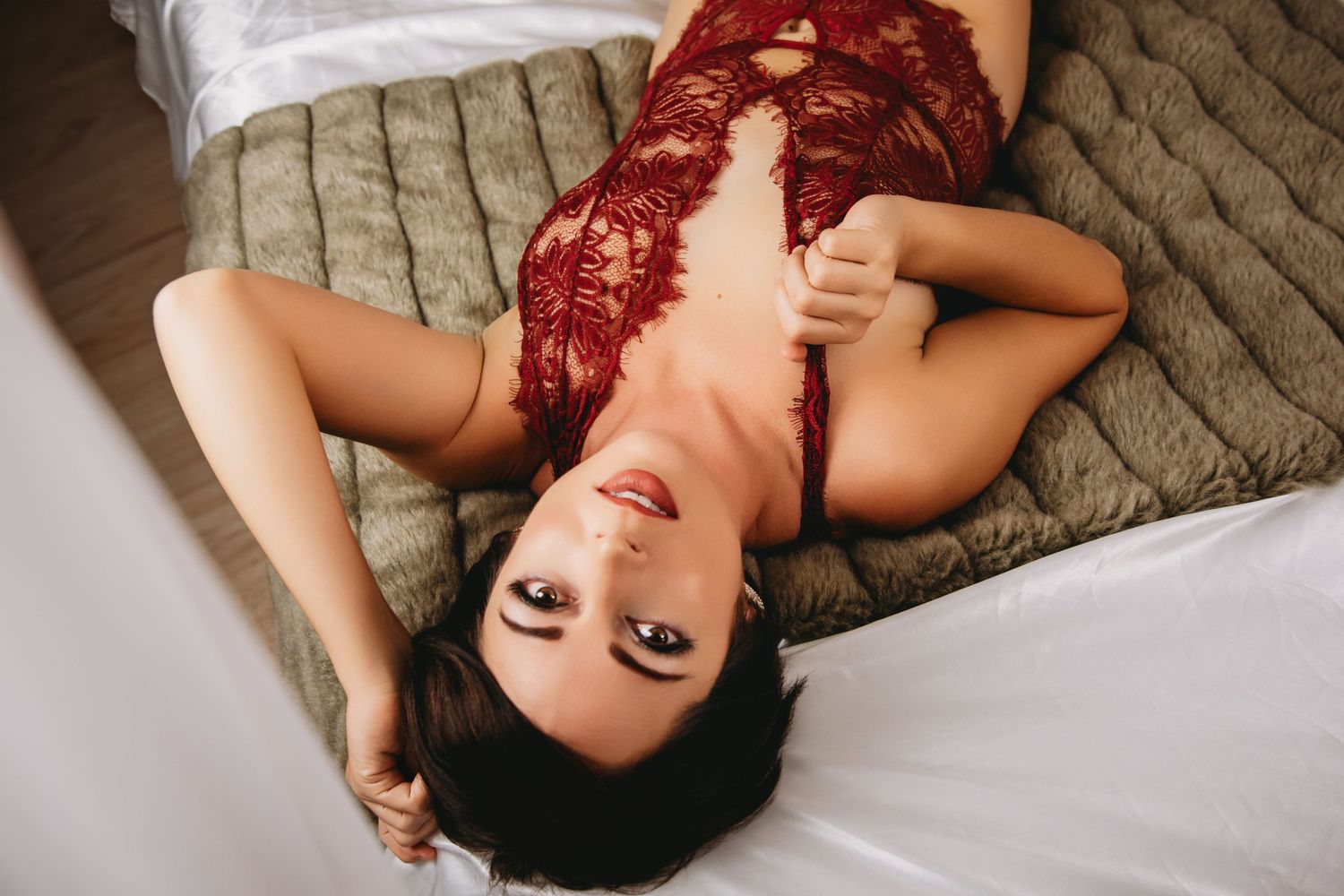 Woman in her 30s with short hair in red lace, lying on a bed in natural light | Venice, FL boudoir photographer