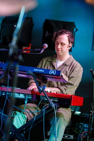 Musician performs on stage with an Arturia keyboard synthesizer in a colorful blue-lit performance setting.