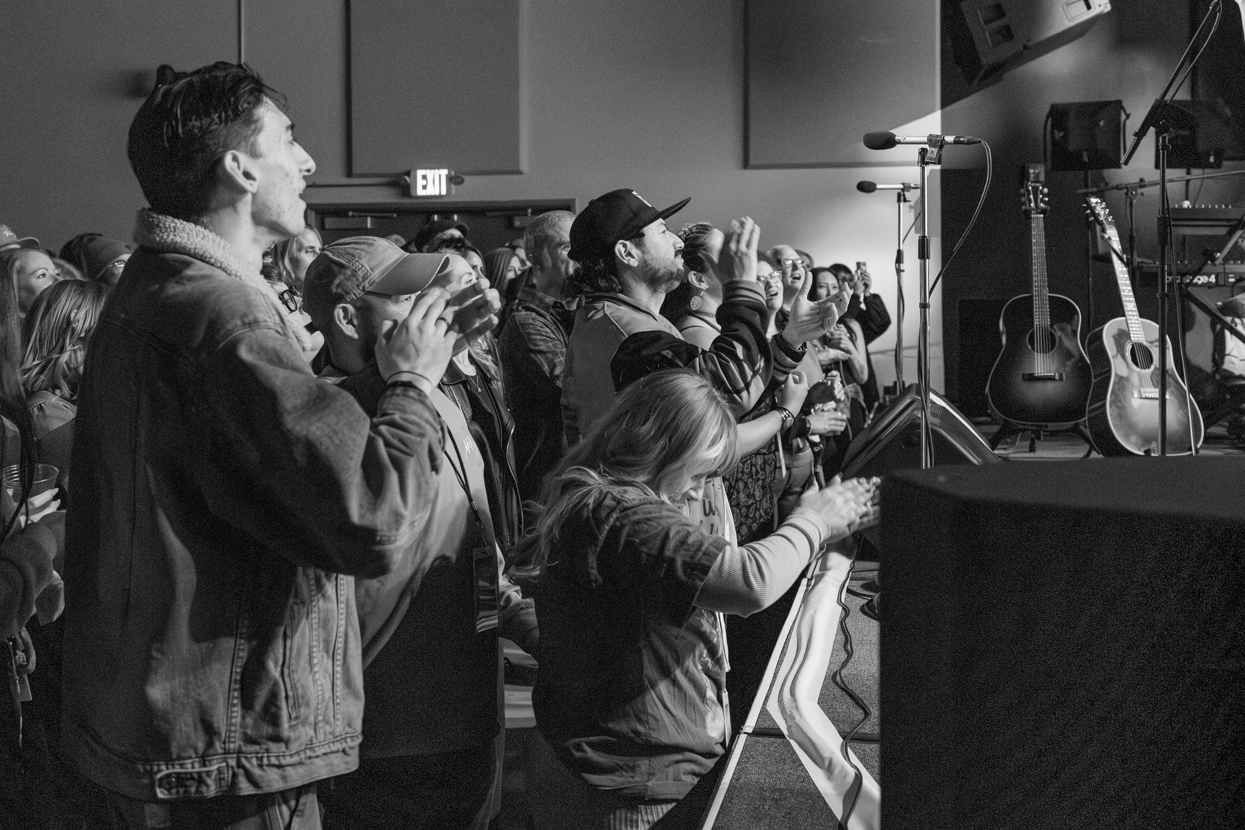 Black and white photo of people in winter coats raising their hands while worshipping at a church service.