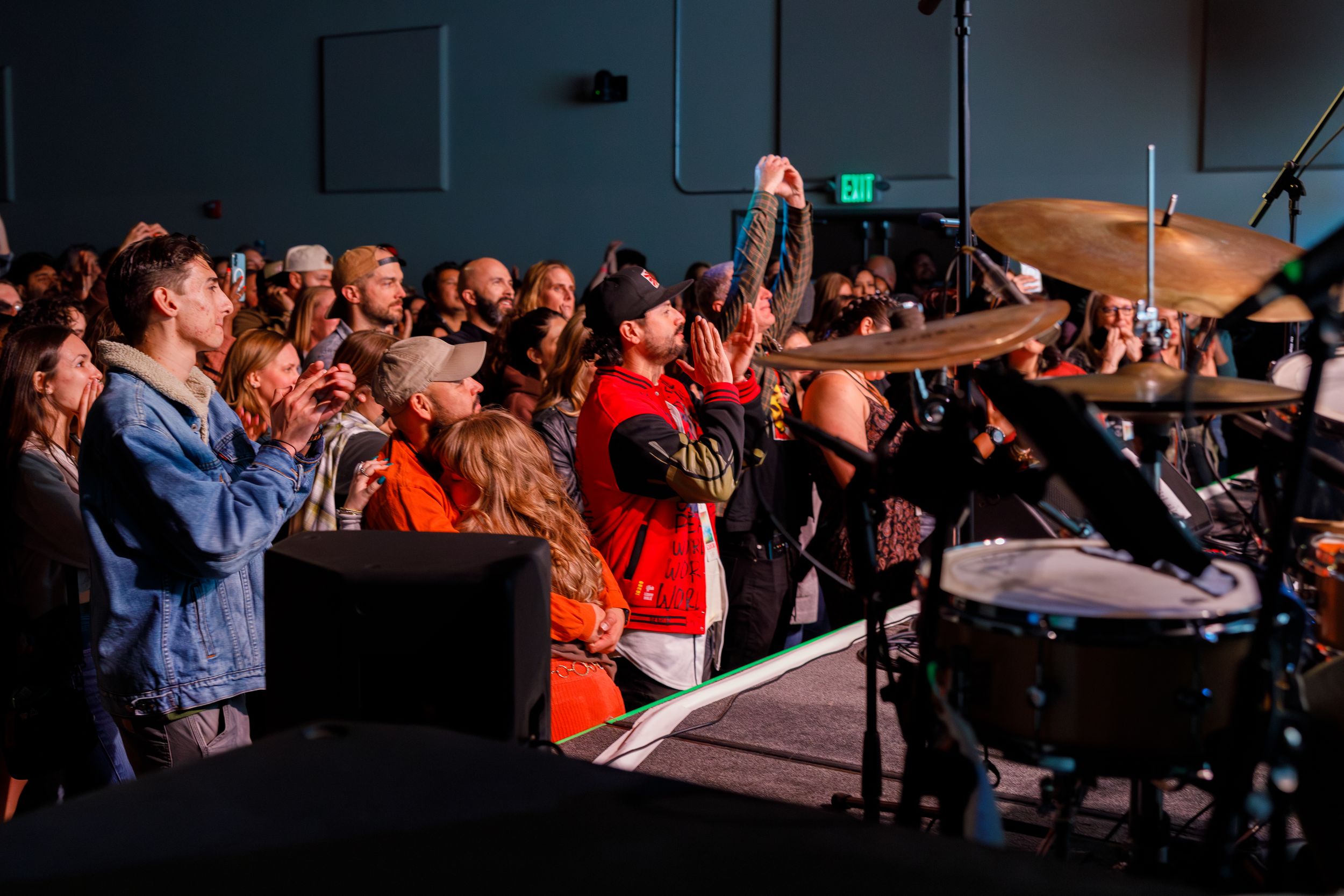 An energetic crowd enjoys a live music performance with musicians on stage in a dimly lit concert venue.