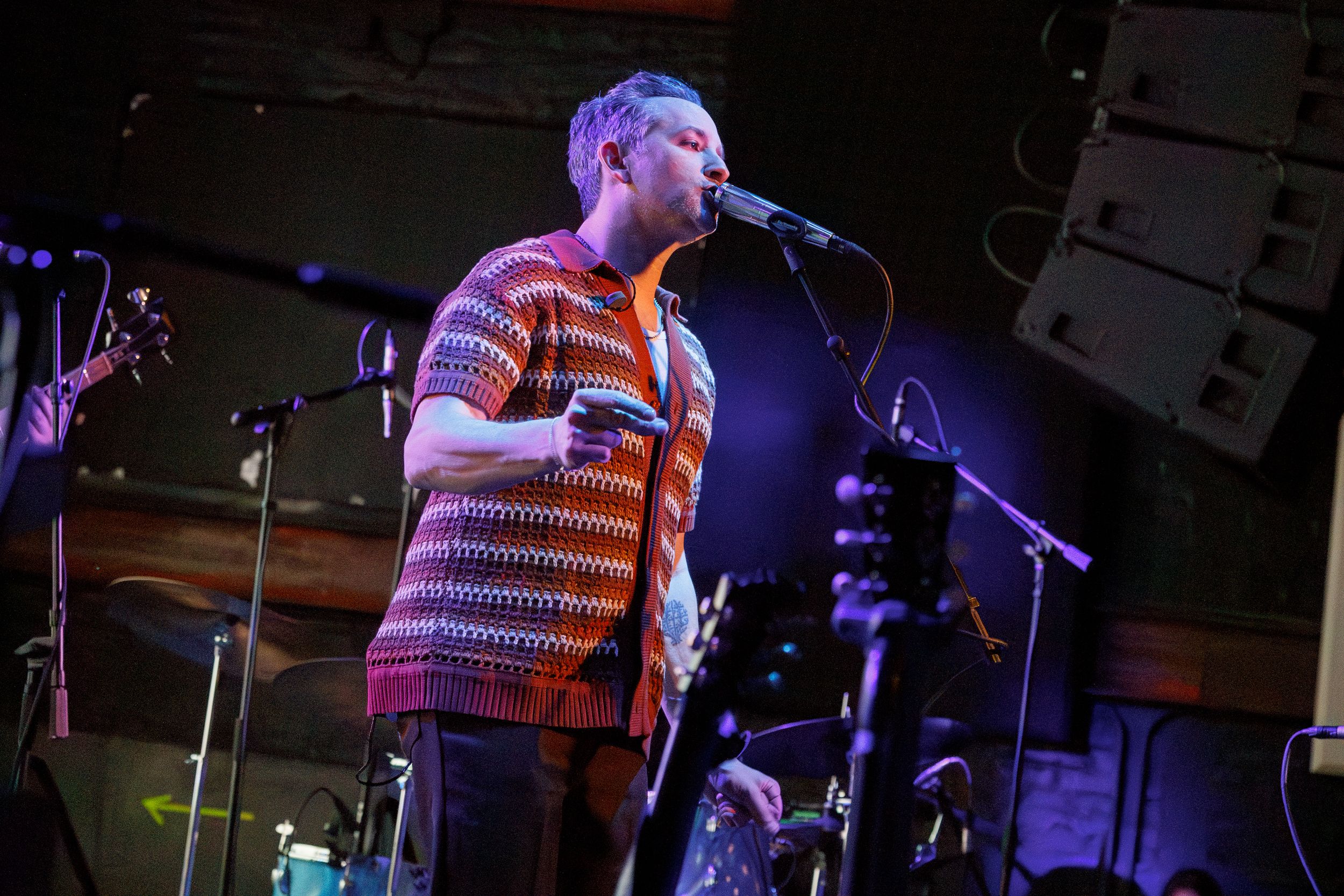Musician performs on stage in a striped knit sweater under dramatic blue lighting at a concert venue.