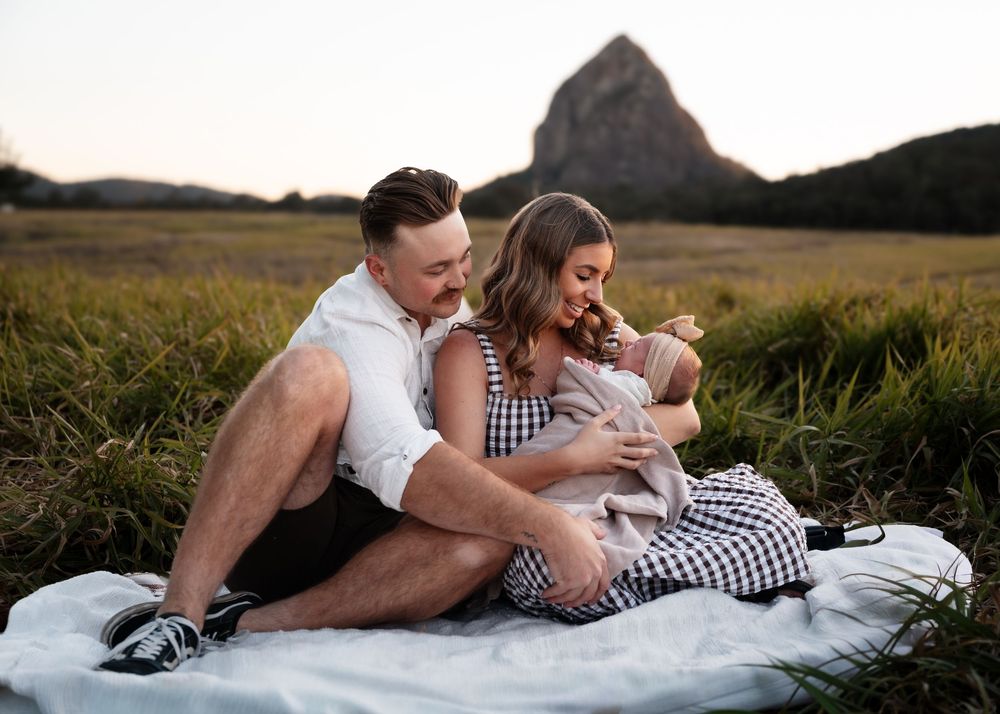 Couple lying on white blanket in grassy field at sunset sharing intimate romantic moments together.