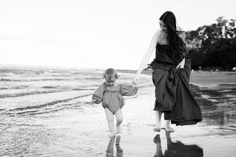 A black and white photo shows a young child running and playing on a beach at the water's edge.