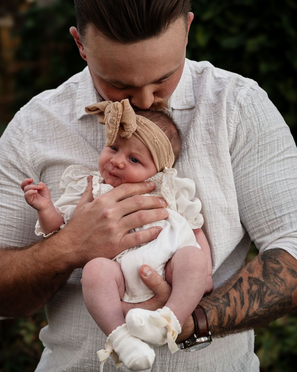 A tender moment captured in black and white as a parent lovingly kisses a baby wearing a white dress.