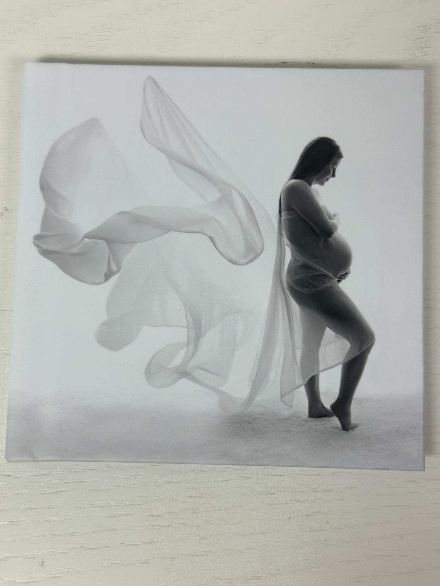 Black and white maternity photo print of pregnant woman with flowing fabric, displayed as a canvas or album print.