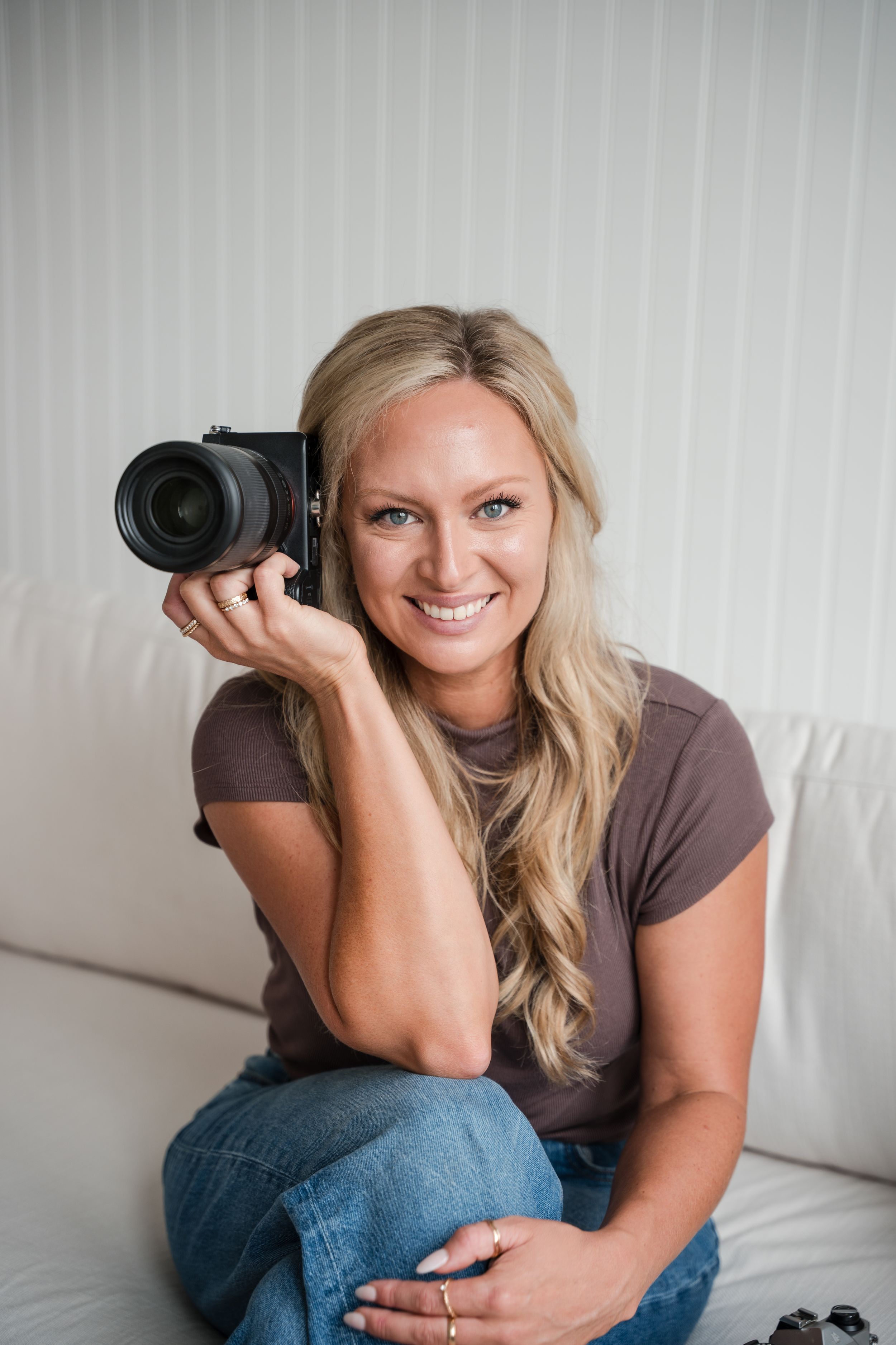 Professional photographer in black dress holding DSLR camera against white background.