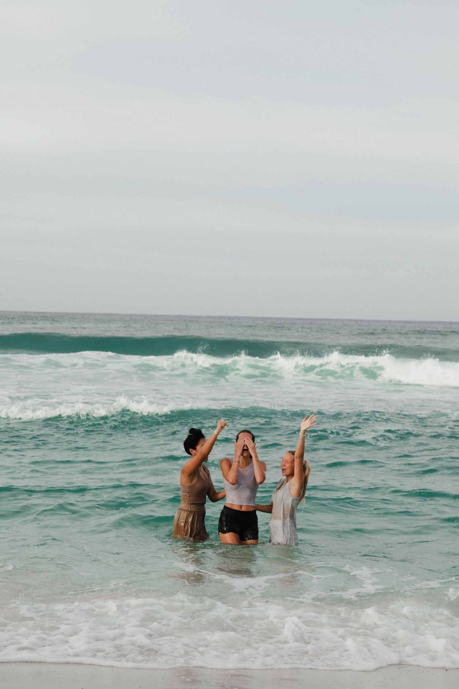 Group of friends playing in ocean waves on sunny beach day.