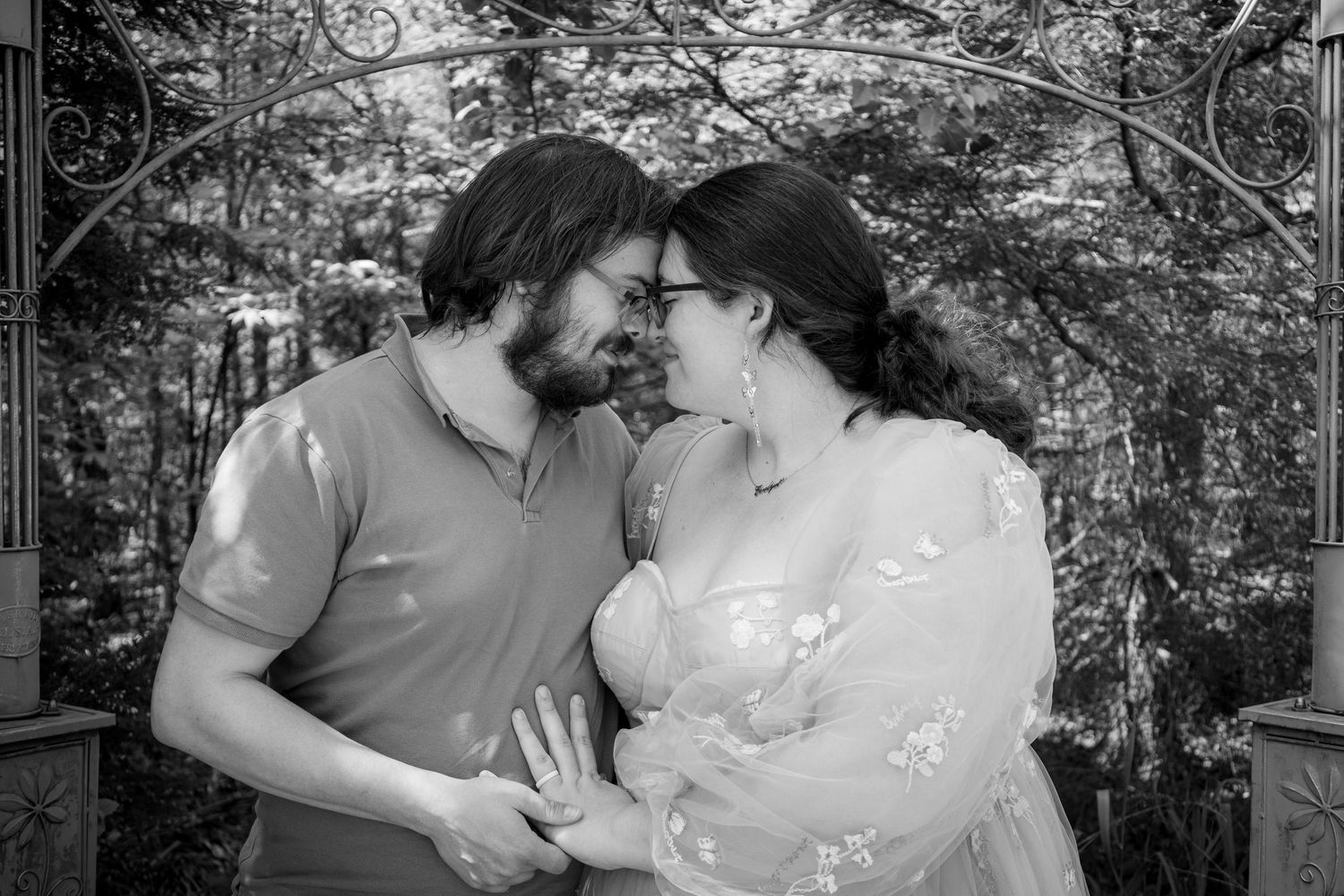 A romantic black and white outdoor portrait of a couple in casual attire sharing an intimate moment in a garden setting.