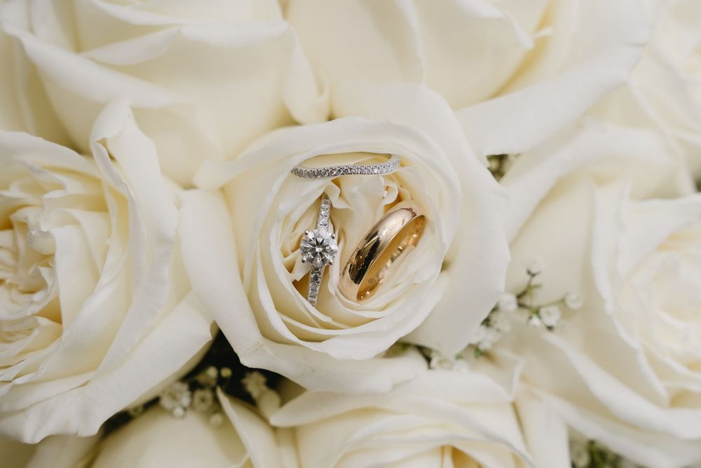 Wedding rings nestled inside a white rose among a bouquet of cream colored roses.