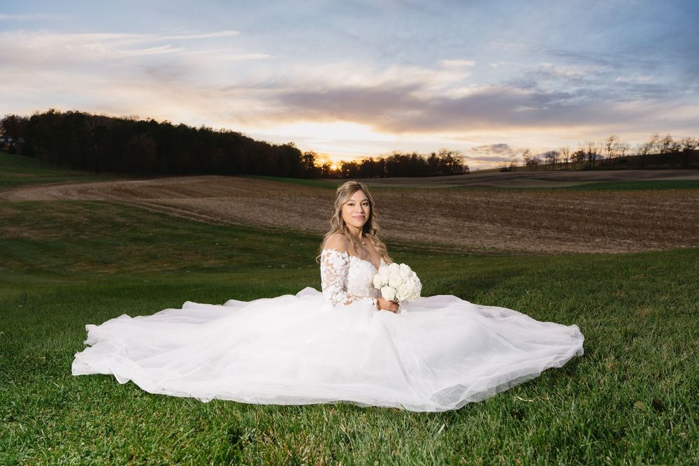 Panoramic view of a sunset wedding celebration in a scenic field with mountains on the horizon.