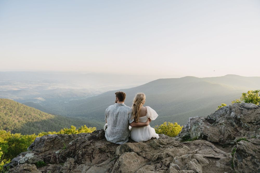 People sitting on mountain overlook enjoying scenic mountain range views at sunset in the distance.