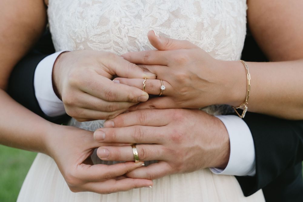 Close-up of hands with wedding rings resting on white formal attire.